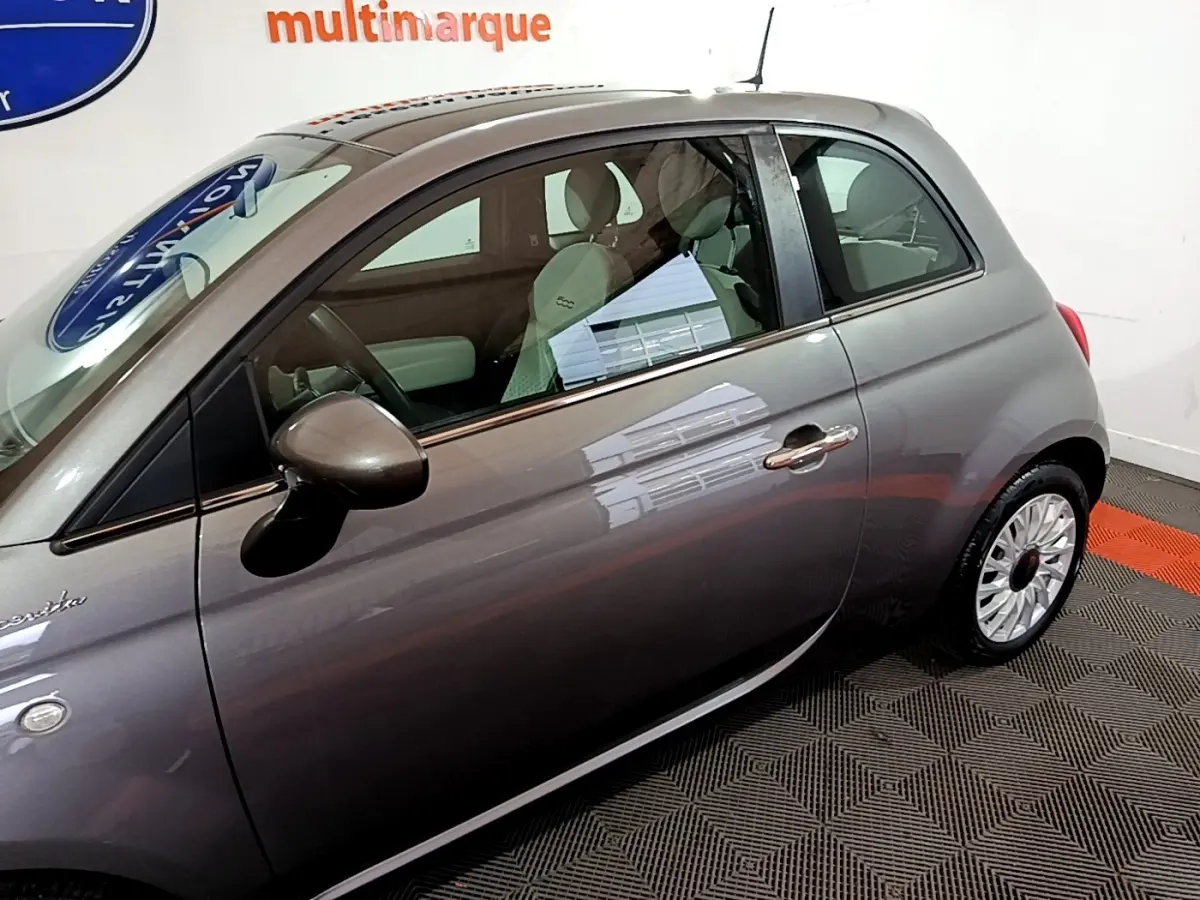 Vue latérale droite d'une FIAT 500 gris foncé 2022 avec rétroviseur et jantes visibles en intérieur showroom.