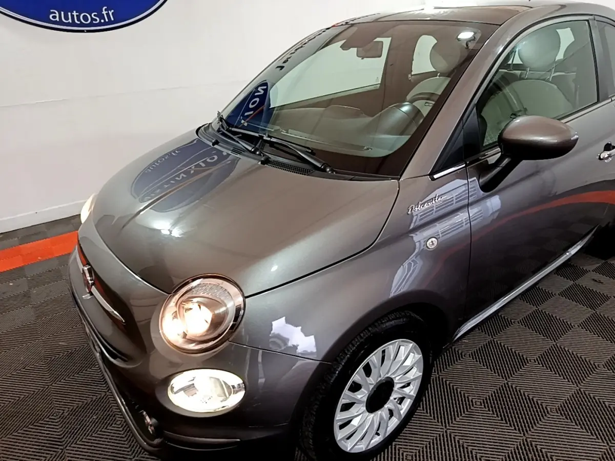Vue 3/4 avant droite d'une FIAT 500 Dolcevita gris foncé avec phares allumés et jantes argentées design.