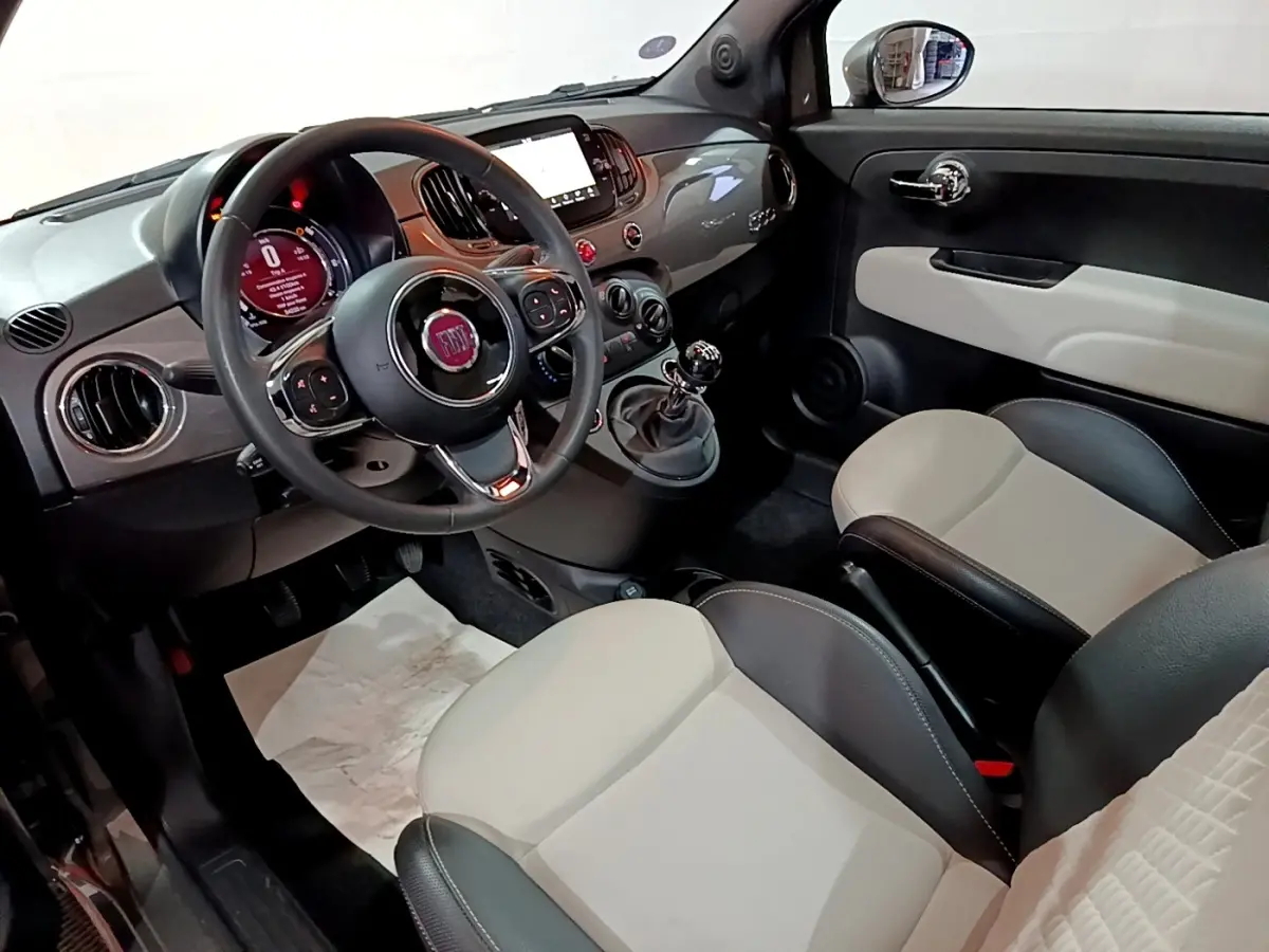 Vue intérieure avant droite de la Fiat 500 1.0 Dolcevita avec tableau de bord gris brillant et sièges bicolores beige et noir.