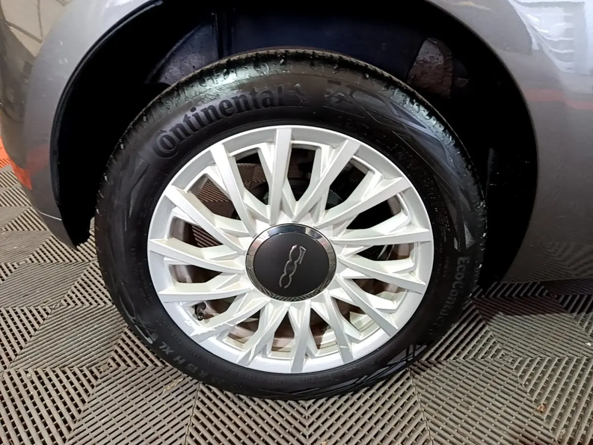 Gros plan sur la roue avant gauche grise d'une FIAT 500 1.0 70ch BSG Dolcevita avec jante argentée à rayons fins.