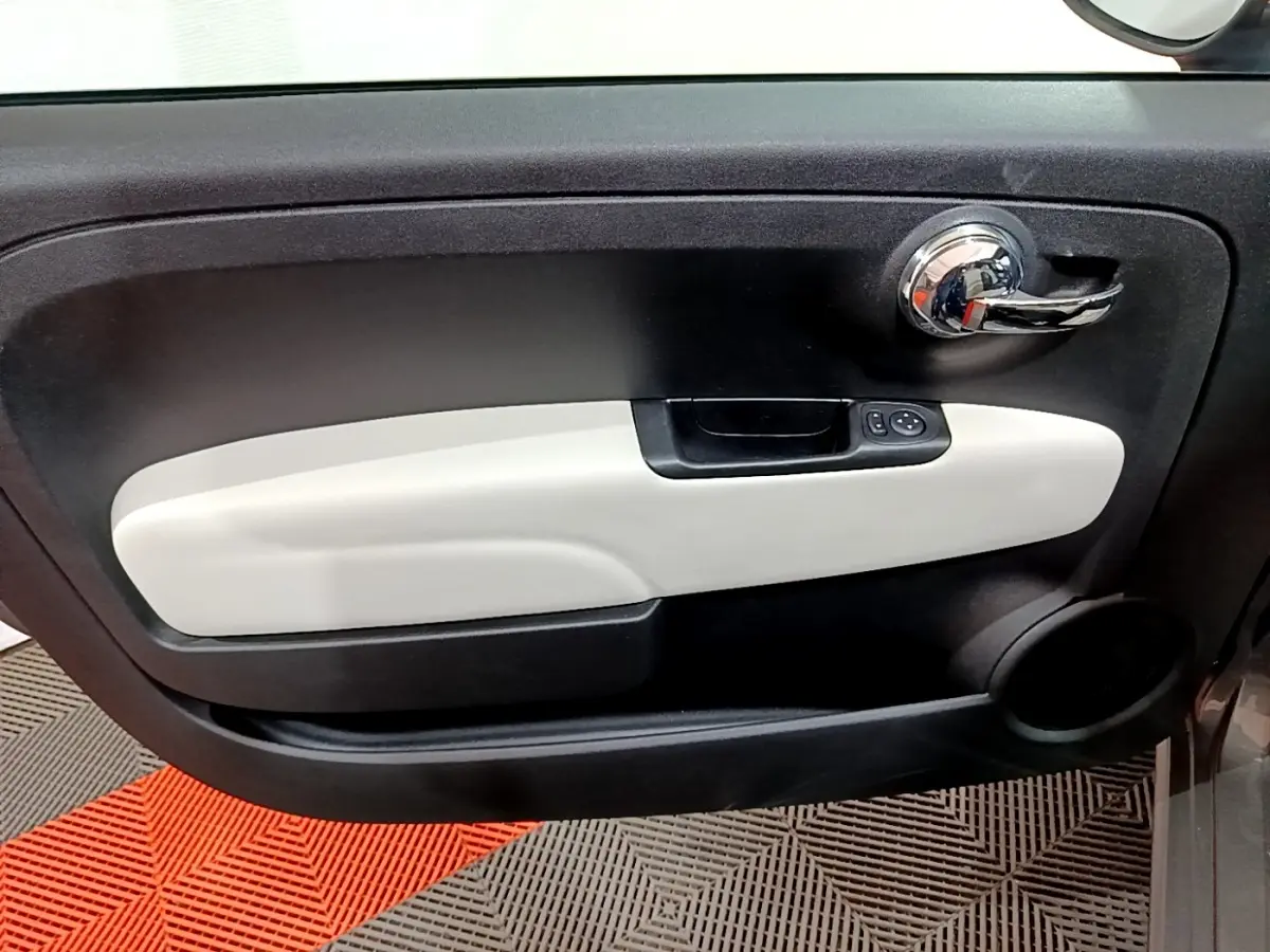 Gros plan sur la porte intérieure côté conducteur de la Fiat 500 gris foncé, avec poignée chromée et insert beige clair.