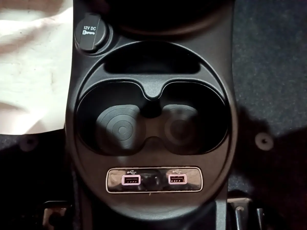 Gros plan sur la console centrale noire de la Fiat 500 avec porte-gobelets, prise 12V et deux ports USB.