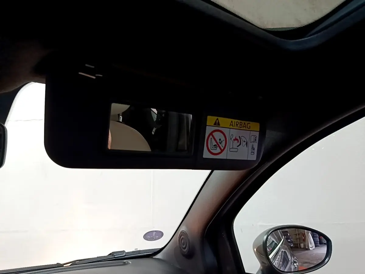 Vue intérieure du pare-soleil côté conducteur avec miroir et avertissement airbag dans une Fiat 500 gris foncé.