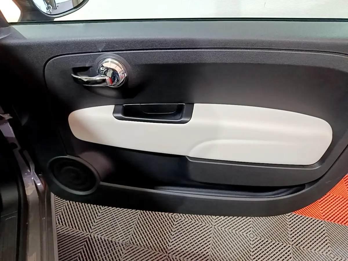 Vue intérieure côté gauche de la porte d’une Fiat 500 gris foncé avec poignée chromée et panneau beige.