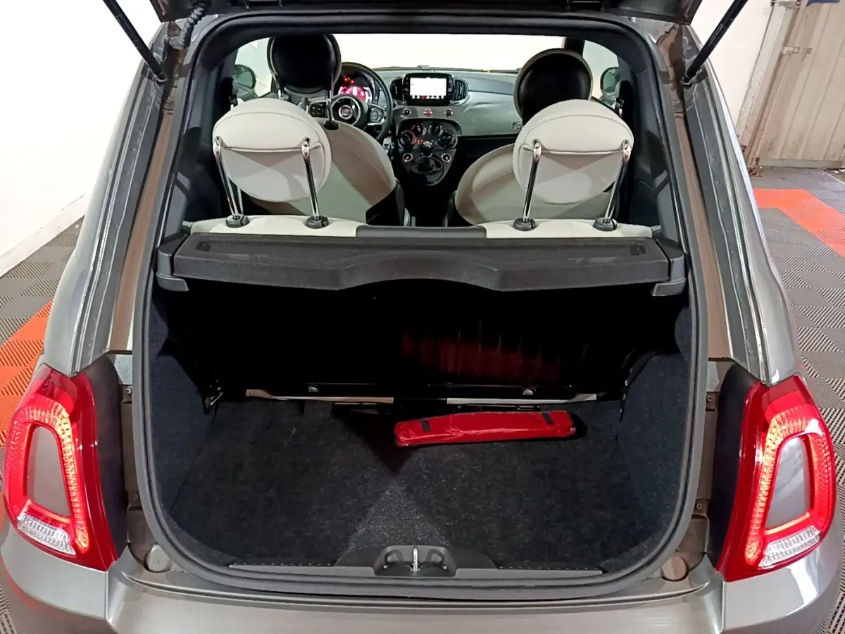 Coffre ouvert d’une FIAT 500 gris foncé vue arrière, montrant l’intérieur avec sièges clairs et tableau de bord tactile.