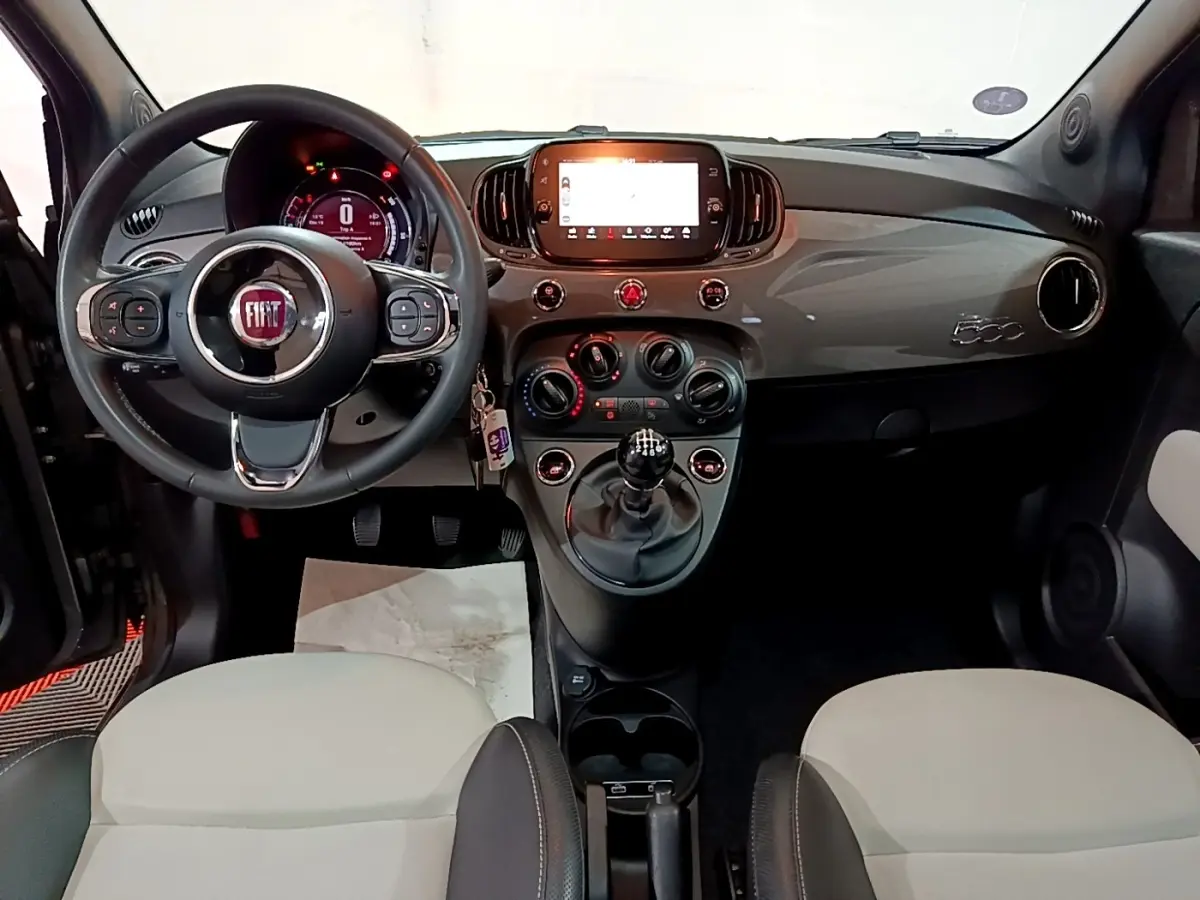 Vue intérieure avant de la Fiat 500 gris foncé 2022, volant cuir, tableau de bord avec écran tactile et boîte manuelle.