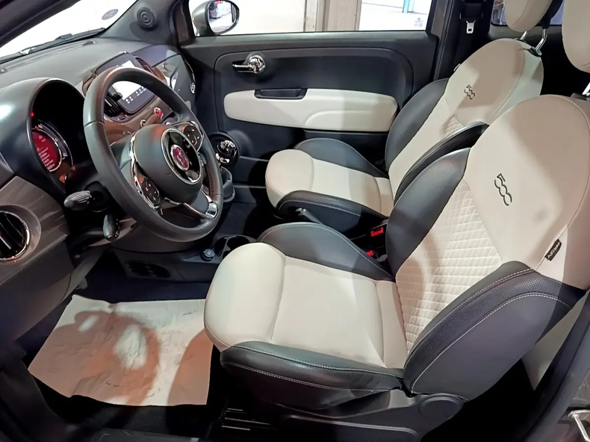 Vue intérieure côté conducteur de la Fiat 500 1.0 gris foncé, sièges bi-ton beige et noir avec logo 500 brodé.