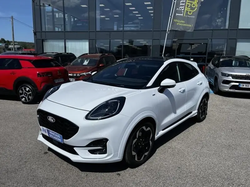 Ford Puma blanc en 3/4 avant droit avec toit noir et jantes noires, stationné devant un showroom.