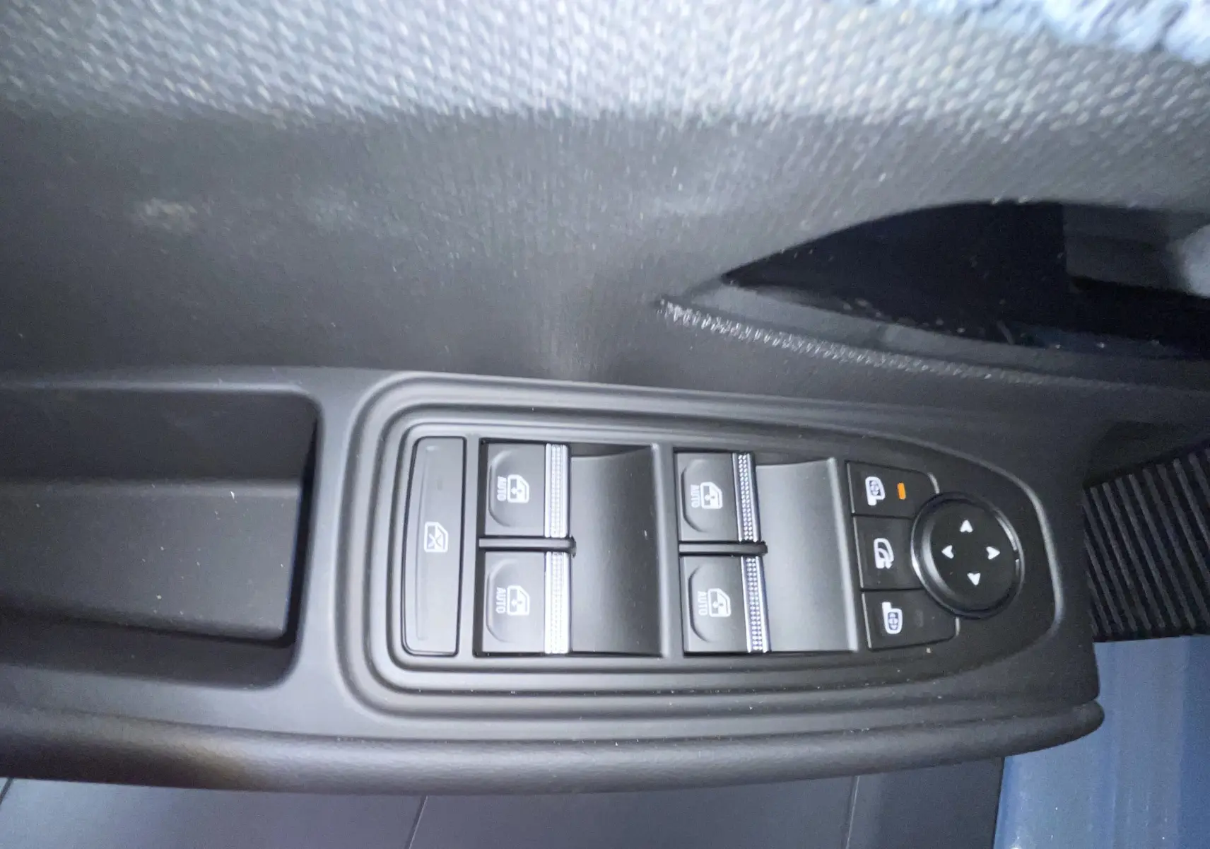 Gros plan sur les commandes des vitres électriques et rétroviseurs côté conducteur d'une Renault Clio gris Rafale métal.