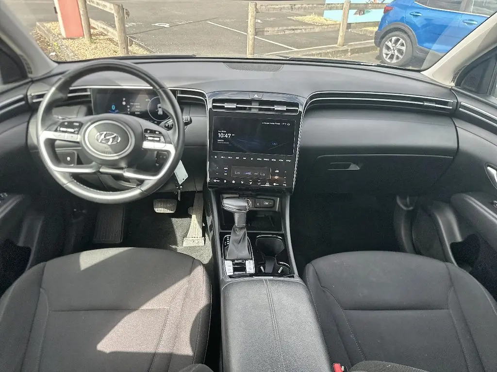 Vue intérieure avant du Hyundai Tucson 2023 gris, montrant le tableau de bord, volant multifonction et console centrale avec écran tactile.