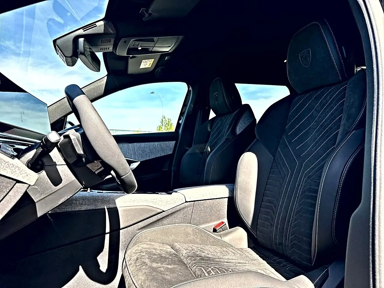 Vue intérieure côté conducteur du Peugeot 5008 Hybrid 145 GT e-dcs6 2025, sièges noirs avec surpiqûres et logo Peugeot.