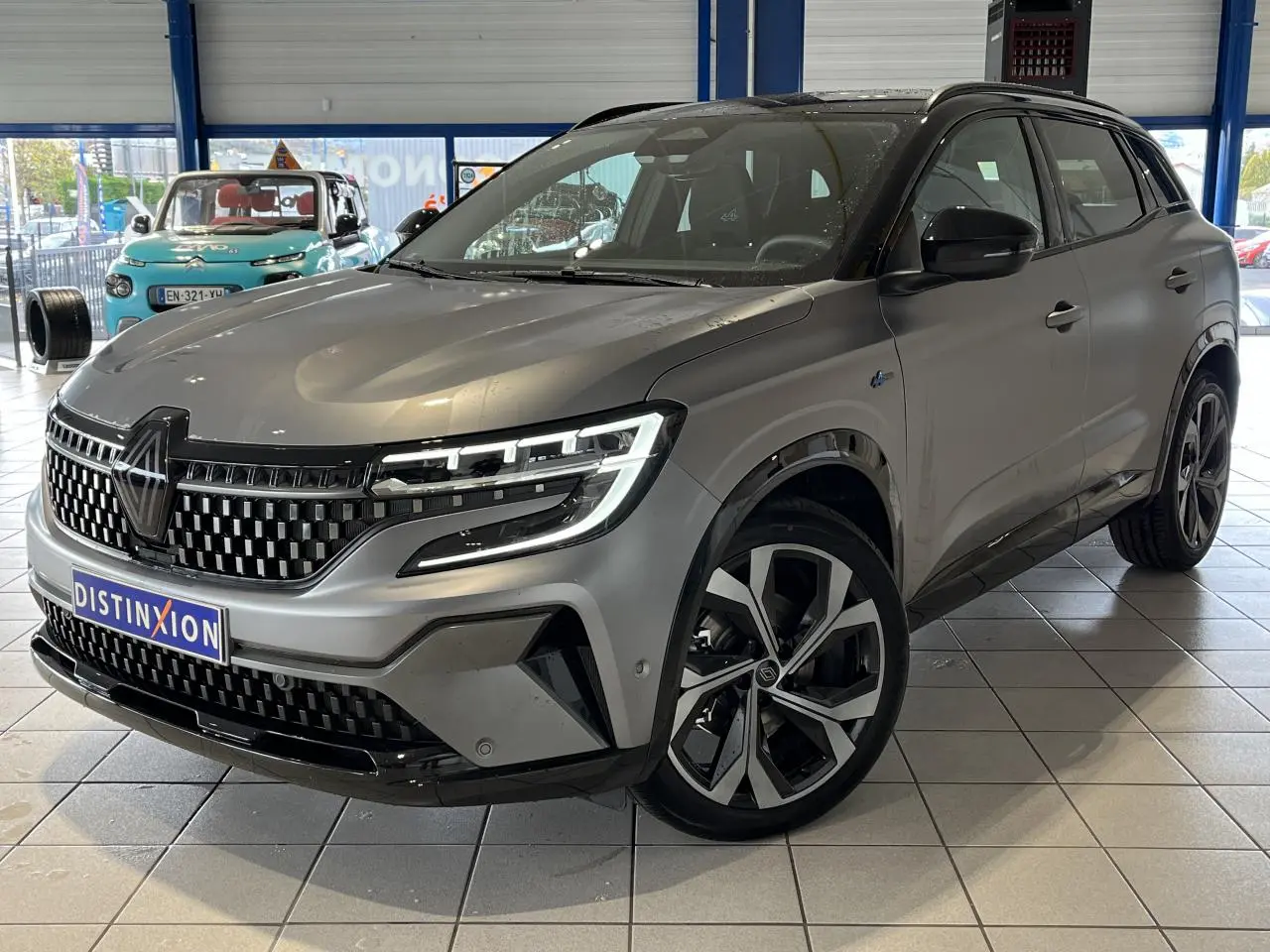 Renault Austral gris 3/4 avant droit en showroom, avec calandre damier ice black et jantes alliage 20 pouces.