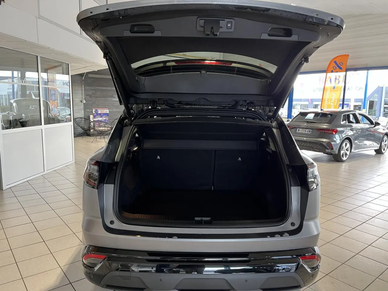 Vue arrière du Renault Austral gris avec hayon motorisé ouvert, montrant le coffre spacieux en intérieur showroom.