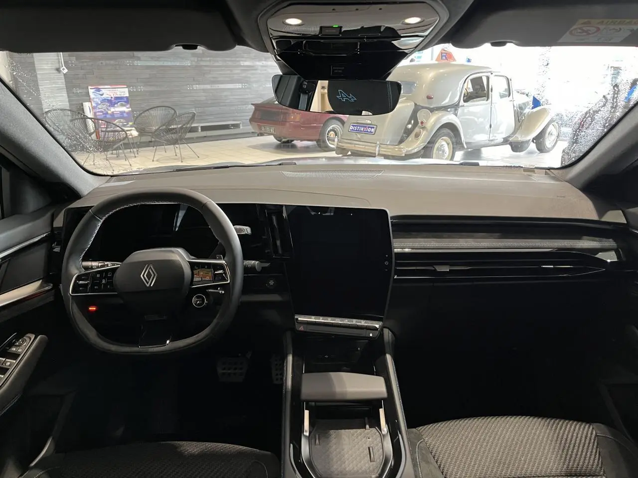 Vue intérieure avant du Renault Austral 2025 gris, avec volant Alcantara, grand écran central vertical et tableau de bord épuré.