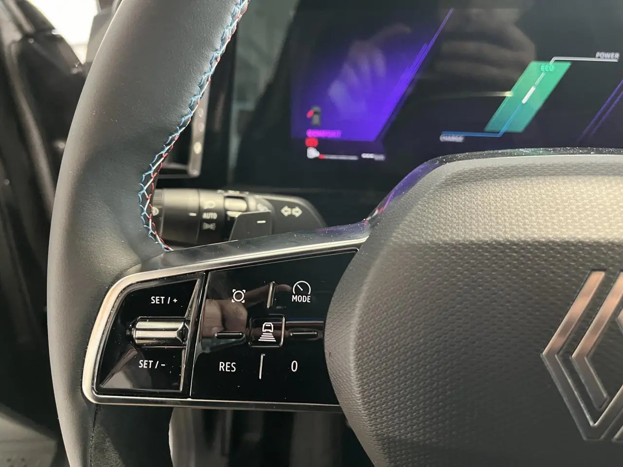 Gros plan sur le côté gauche du volant gris avec surpiqûres bleues et commandes de régulateur du Renault Austral 2025.