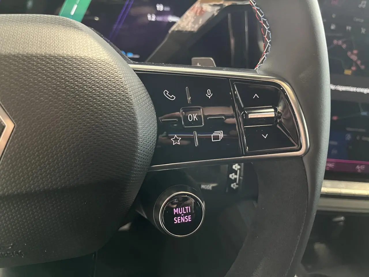 Gros plan sur le volant Alcantara du Renault Austral gris, avec commandes multifonctions et bouton Multi-Sense éclairé.