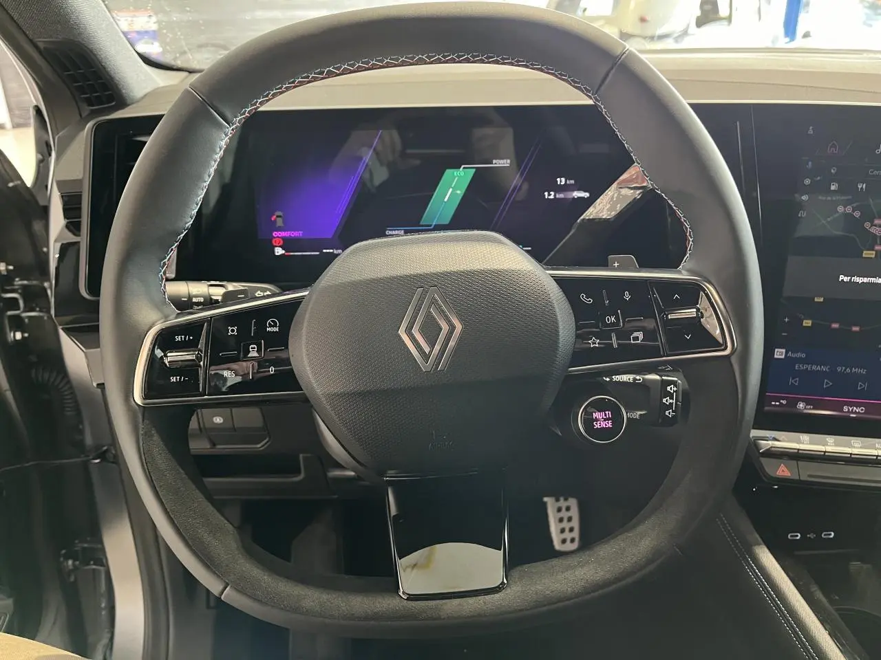 Vue rapprochée du volant en textile et Alcantara avec logo Renault, tableau de bord numérique et écran tactile du Renault Austral 2025.