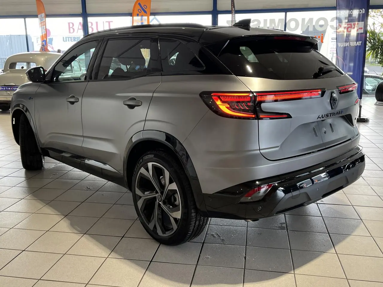 Vue 3/4 arrière droite du Renault Austral gris avec feux LED allumés et jantes alliage 20 pouces en intérieur showroom.