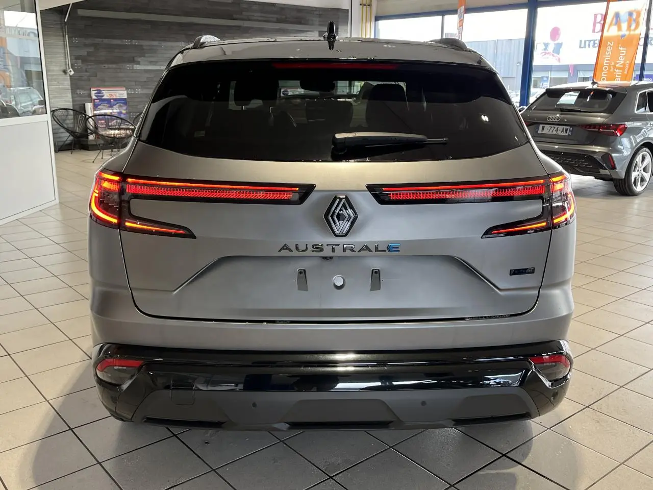 Vue arrière du Renault Austral gris avec feux LED allumés et hayon motorisé dans un showroom.