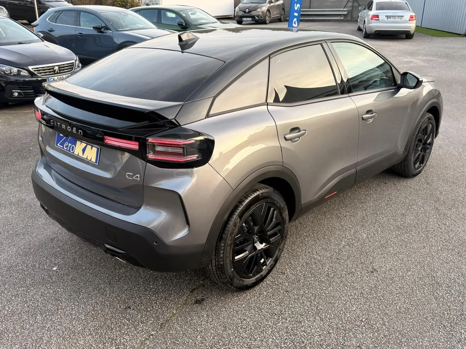 Vue 3/4 arrière droite d'une Citroën C4 hybride 2025 gris Mercury avec toit noir et jantes noires distinctives.