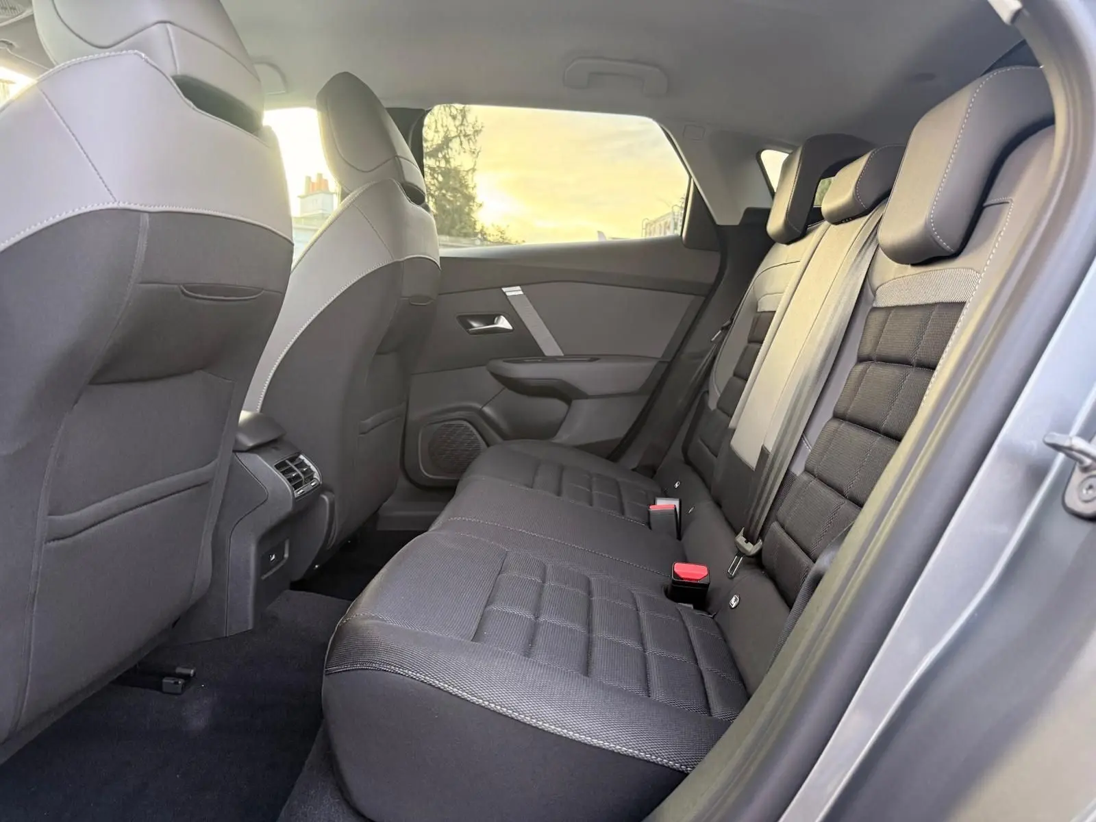 Vue intérieure côté droit des sièges arrière noirs et gris du Citroën C4 hybride 2025 en gris Mercury, avec ceinture et appuie-têtes visibles.