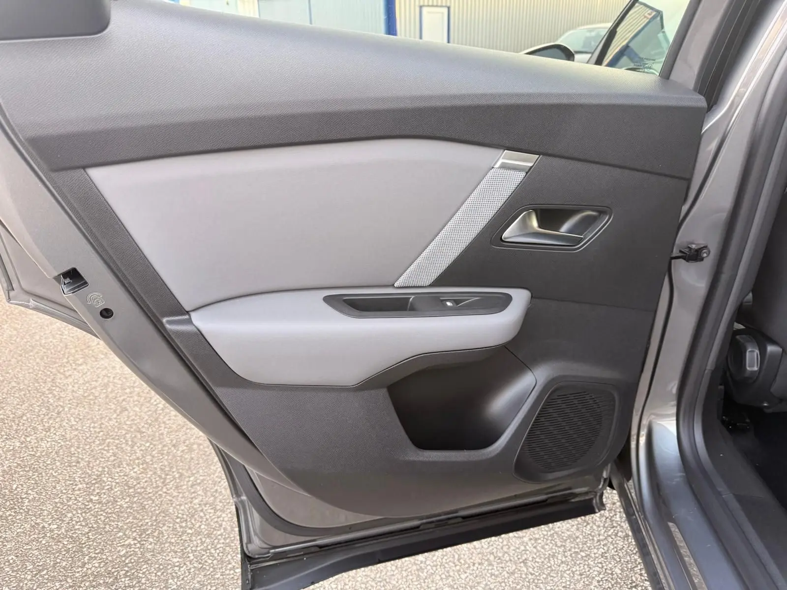 Vue intérieure sur la porte arrière droite gris Mercury du Citroën C4 hybride 2025 avec habillage bicolore et haut-parleur intégré.