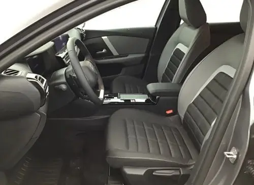 Vue intérieure côté conducteur de la Citroën C4 hybride 2025, sièges gris et console centrale moderne.