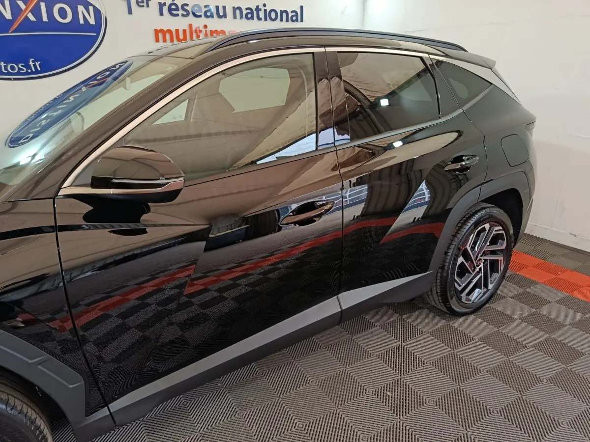 Vue latérale côté gauche du Hyundai Tucson 1.6 Hybrid noir 2025 avec jantes alliage et rétroviseur chromé.