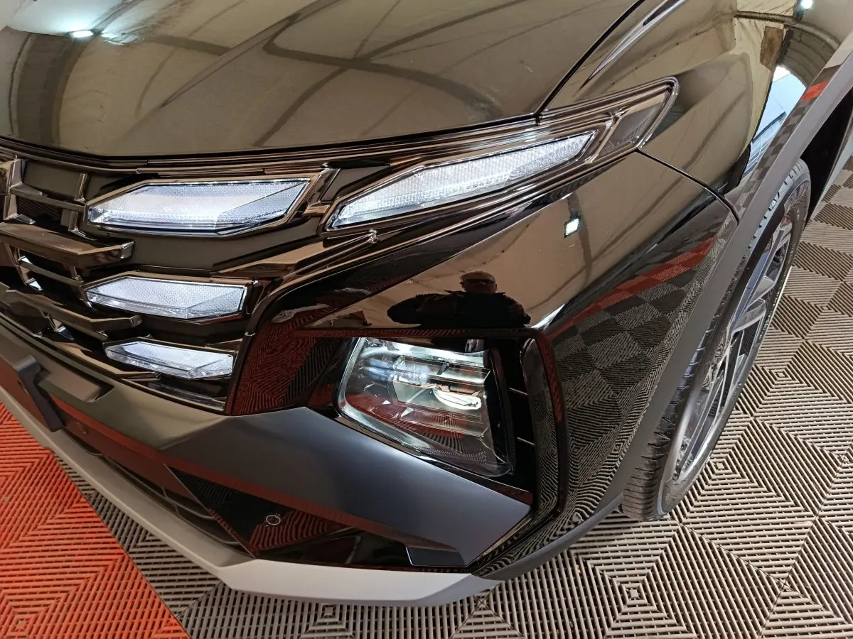 Gros plan sur l'avant droit noir brillant du Hyundai Tucson 2025, mettant en valeur ses phares LED et la calandre distinctive.