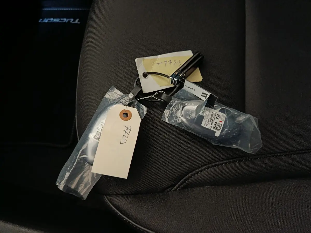 Clé de voiture Hyundai Tucson 1.6 Hybrid posée sur siège tissu noir avec tapis marqué Tucson visible en arrière-plan.