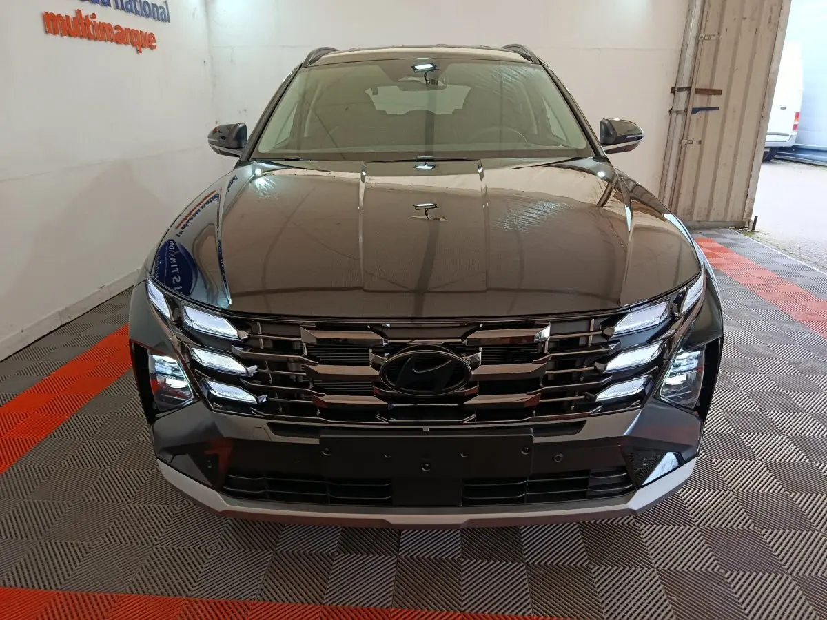 Vue avant d’un Hyundai Tucson 2025 noir avec calandre chromée et feux LED allumés en intérieur showroom.