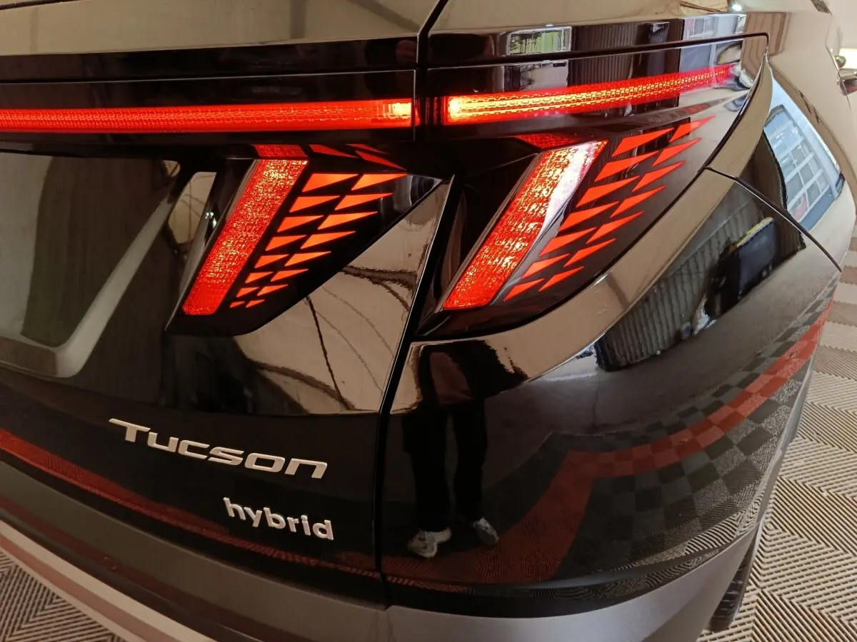 Gros plan sur le feu arrière droit rouge du Hyundai Tucson noir hybride avec logo et nom du modèle visibles.