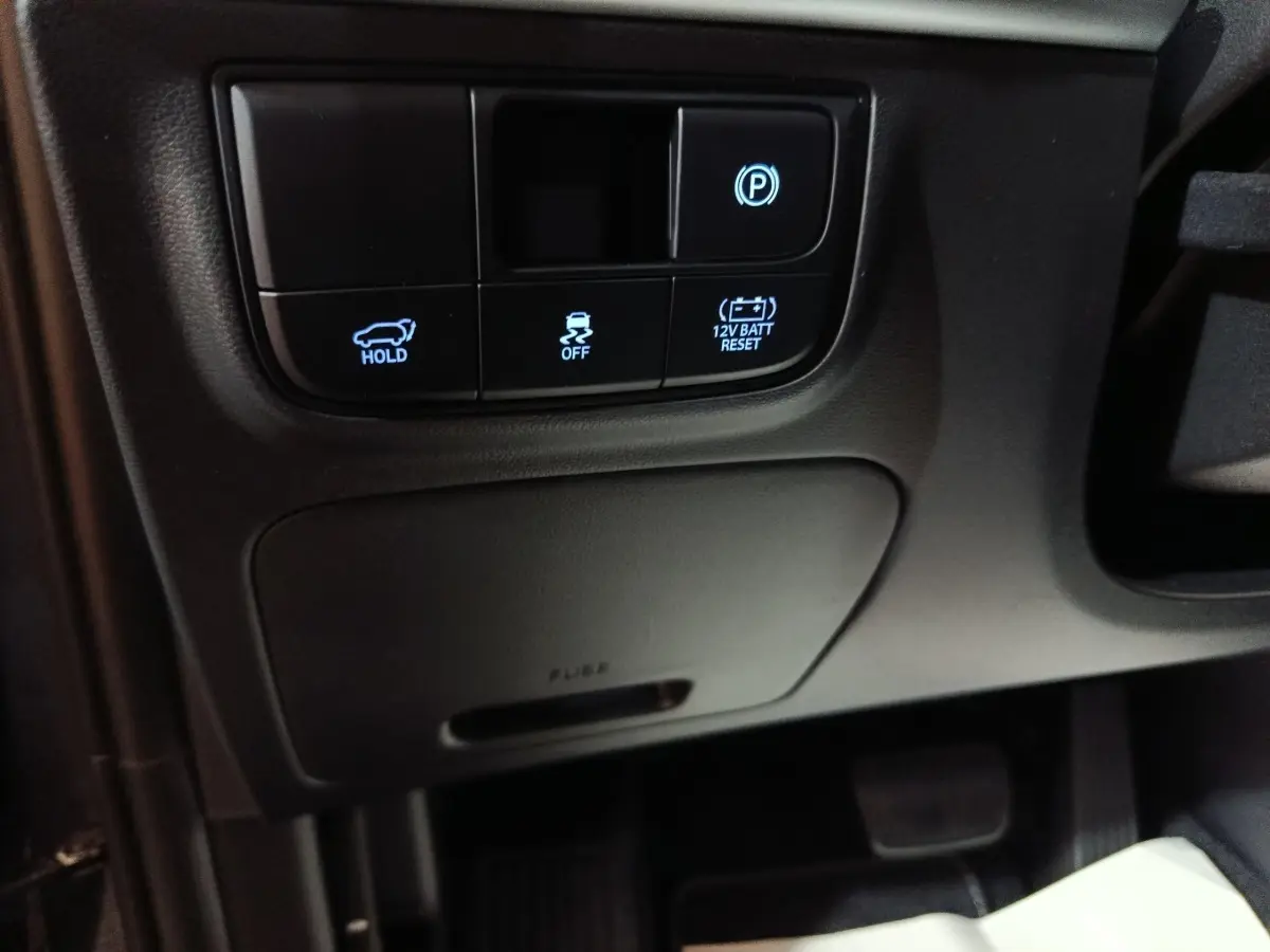 Gros plan sur les commandes noires sous le tableau de bord côté gauche du Hyundai Tucson 1.6 Hybrid 239 Creative Auto 2025.