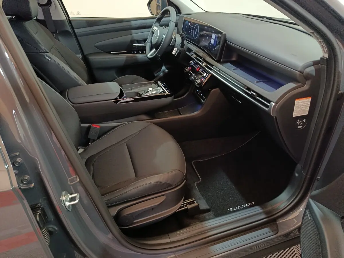Vue intérieure côté conducteur du Hyundai Tucson 2025 noir, avec tableau de bord numérique et sièges en tissu noir.