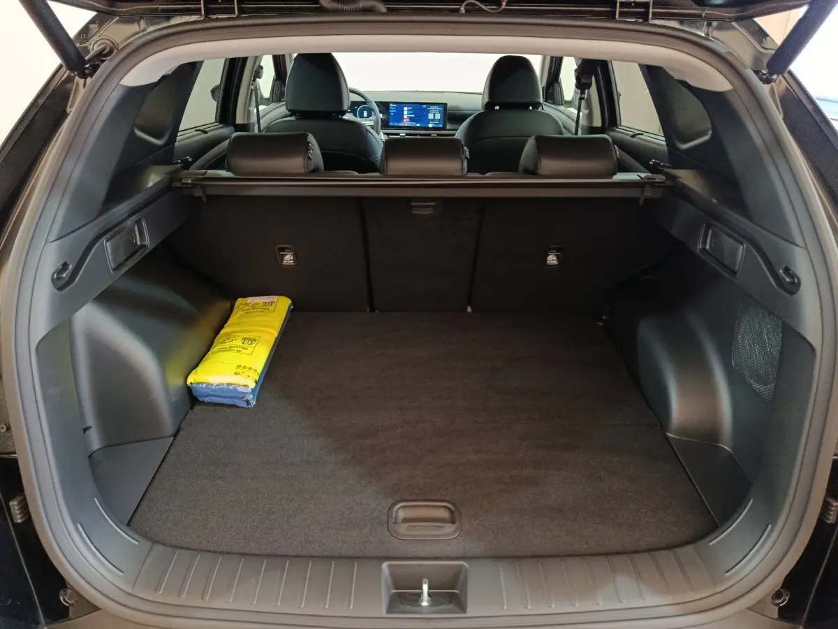 Coffre ouvert vu de l'arrière d'un Hyundai Tucson noir 2025, avec tablette cache-bagages et écran tactile visible.