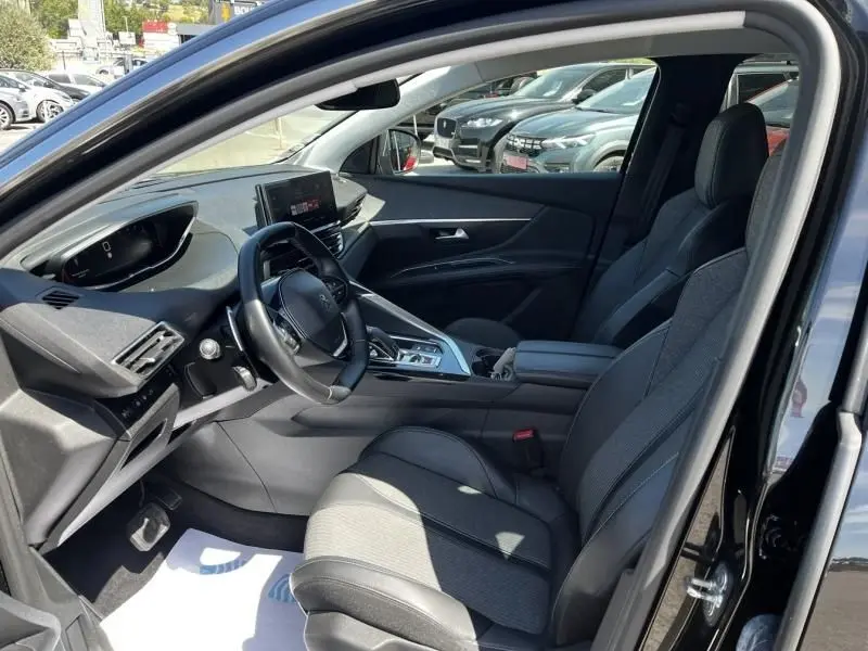 Vue intérieure côté conducteur du Peugeot 3008 noir 2021, mettant en valeur le tableau de bord moderne et les sièges en tissu.