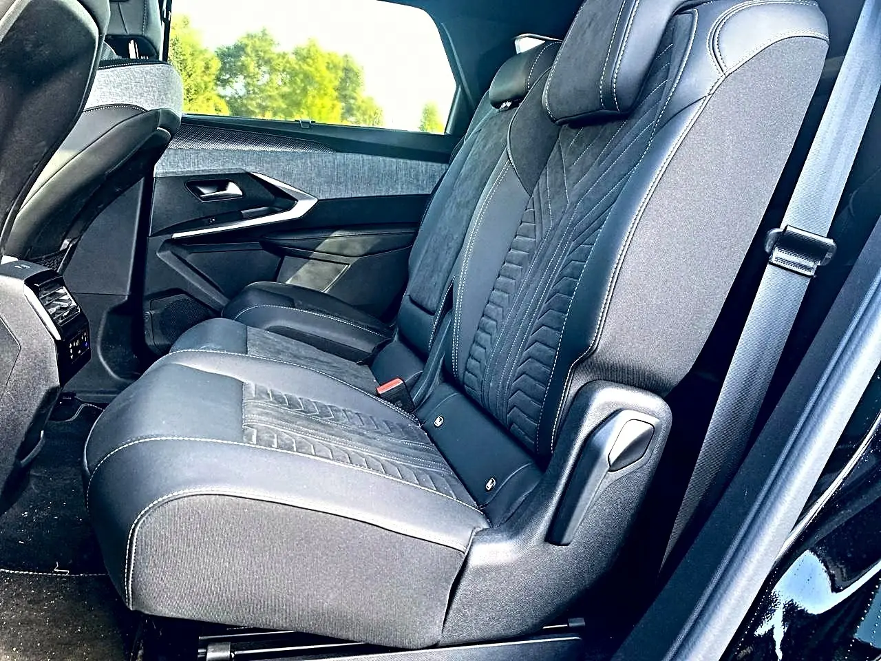 Vue latérale des sièges arrière noirs en tissu et cuir du Peugeot 5008 Hybrid 145 GT 2025 avec appuie-tête et ceinture.