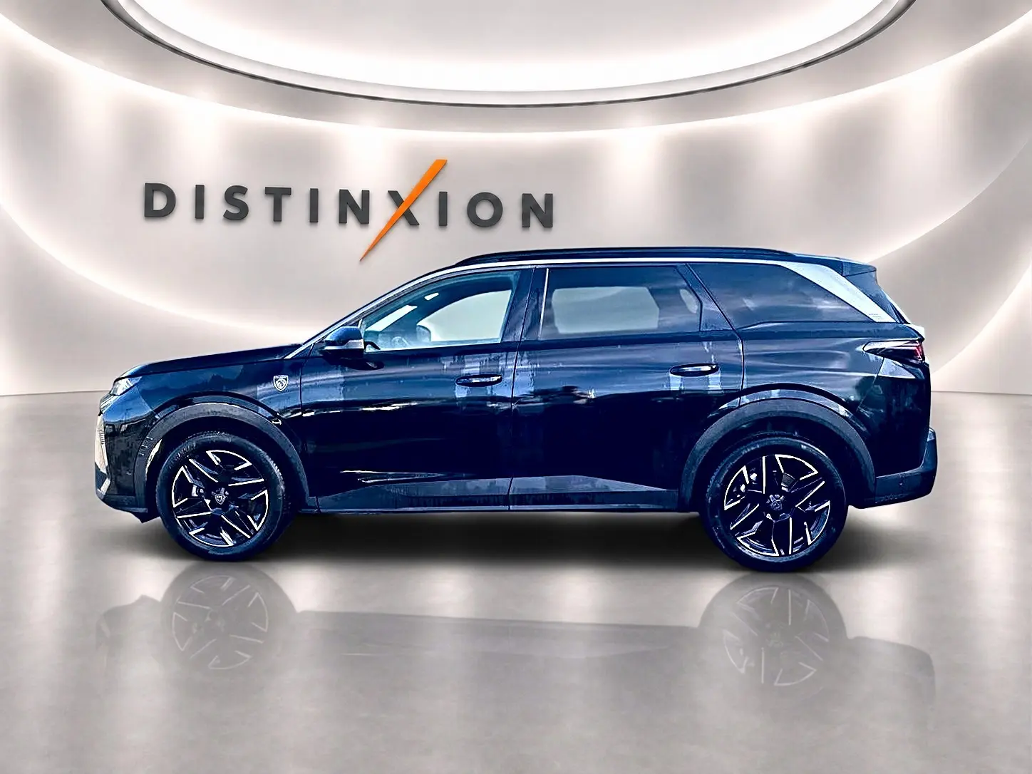 Peugeot 5008 Hybrid 145 GT noir, vue profil droit en intérieur avec jantes alliage et logo Distinxion en arrière-plan.