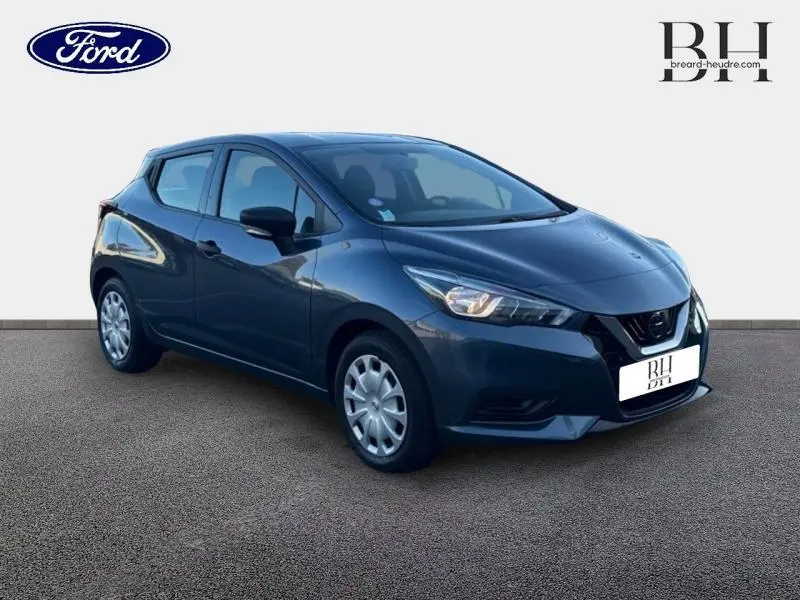 Nissan Micra gris acier vue 3/4 avant droit, avec jantes acier et feux avant allumés sur fond neutre.