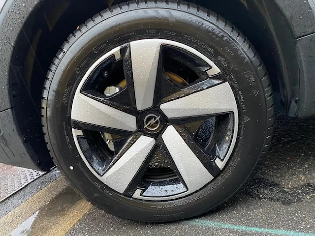 Gros plan sur la roue avant gauche de l’Opel Crossland gris métallisé avec jante alliage bicolore et gouttes d’eau visibles.