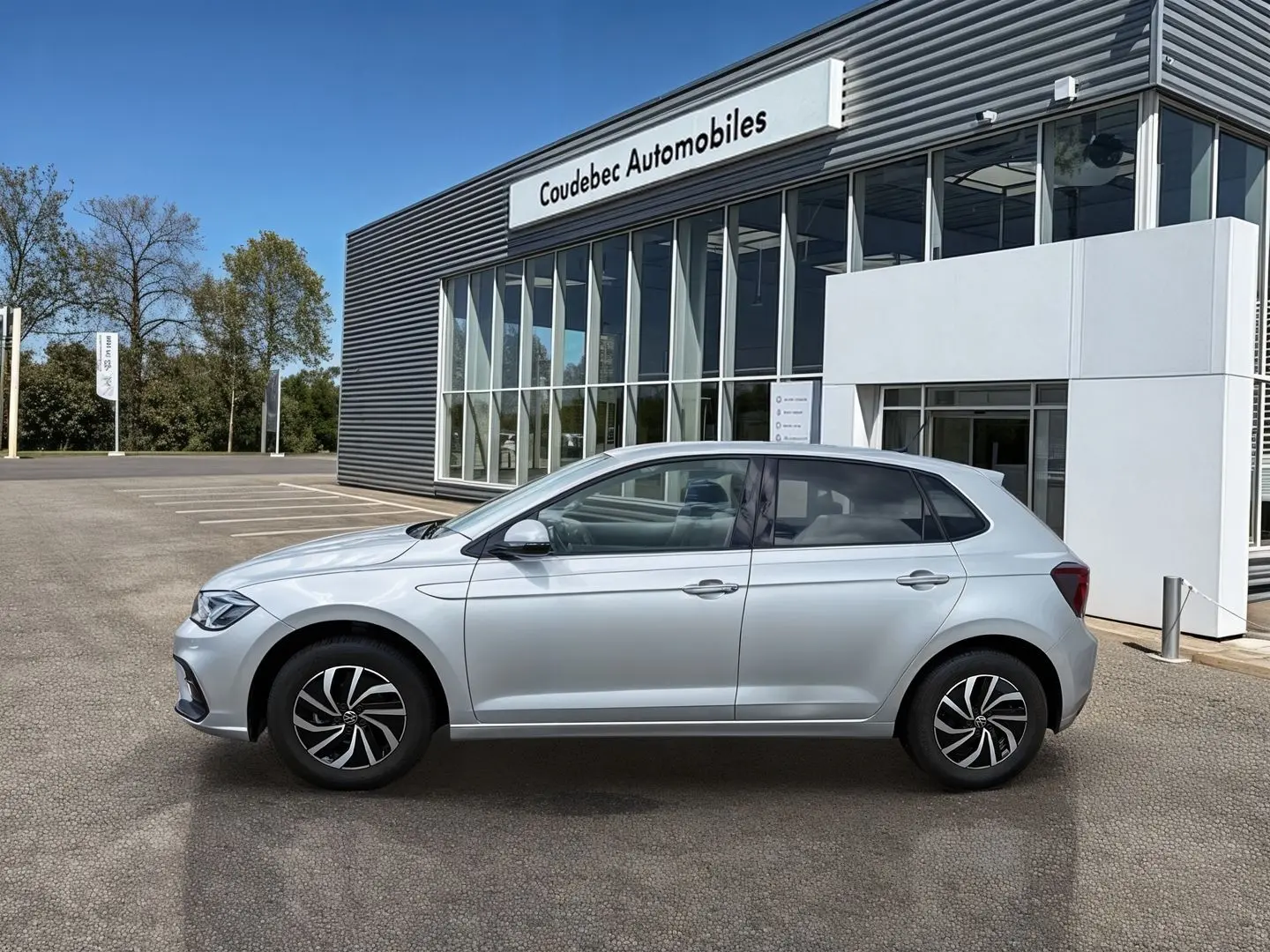 Vue latérale droite d'une Volkswagen Polo grise 2025 garée devant un bâtiment de concession automobile.