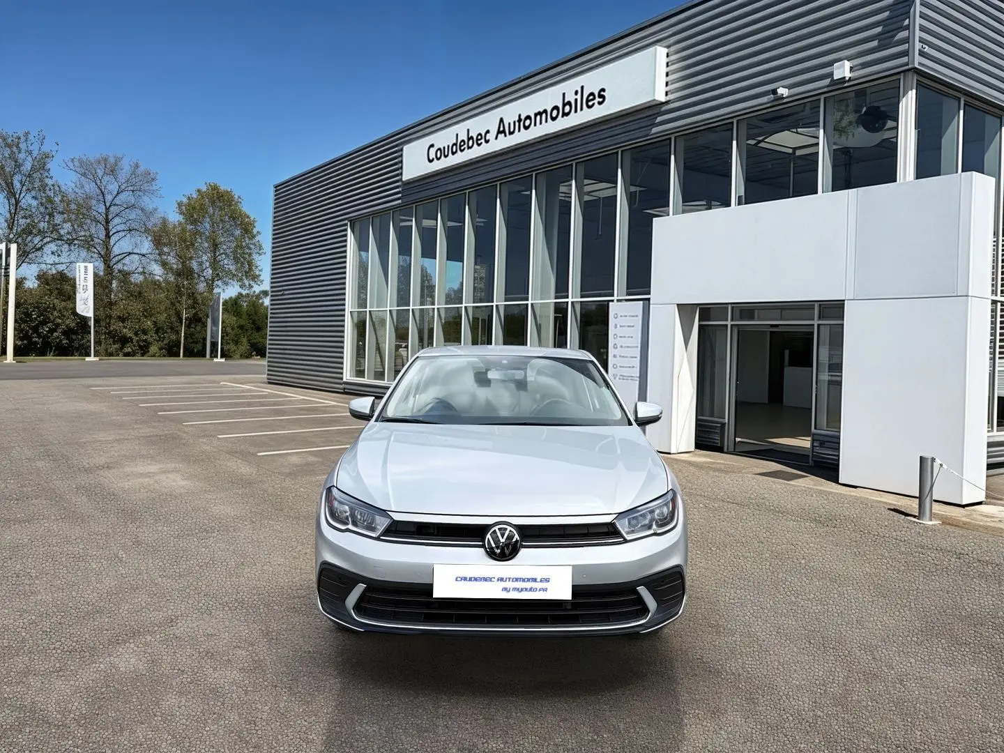Vue de face d'une Volkswagen Polo grise 2025 avec feux LED, stationnée devant un bâtiment de concession automobile.