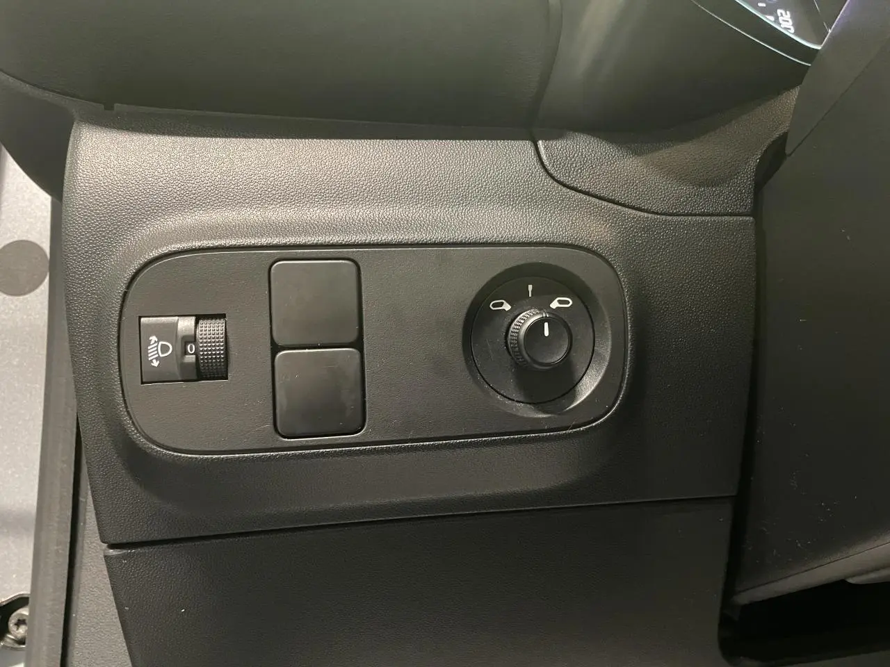 Vue rapprochée des commandes de réglage des phares et des rétroviseurs côté gauche d'une Citroën C3 gris foncé 2024.