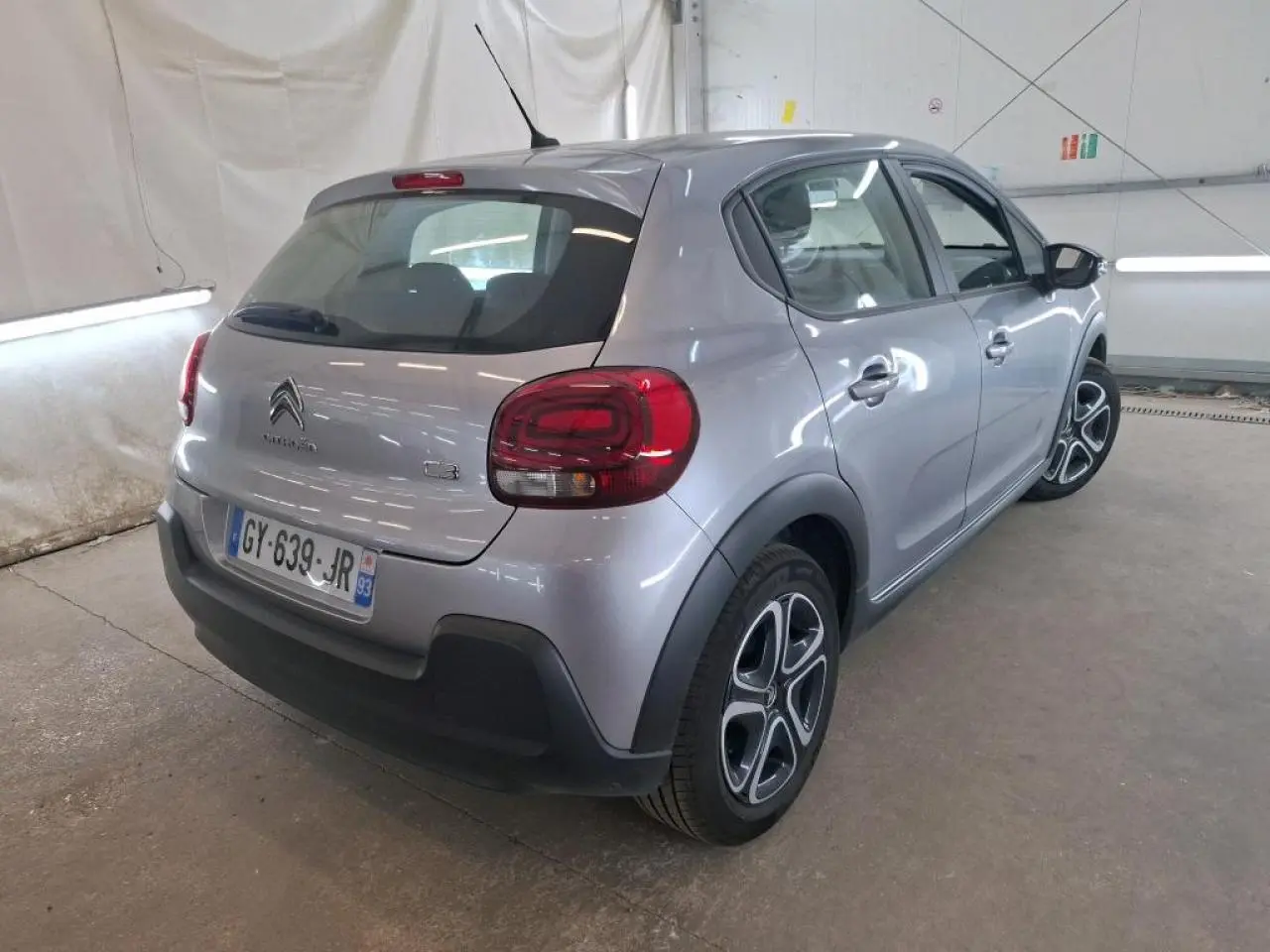 Vue 3/4 arrière droite d'une Citroën C3 gris foncé 2024 avec feux arrière arrondis et jantes distinctives.