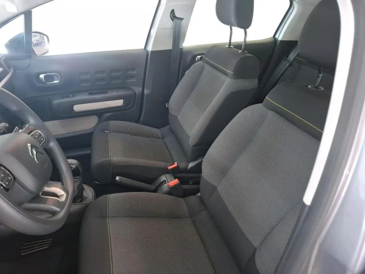Vue intérieure côté conducteur de la Citroën C3 2024 gris foncé, montrant les sièges avant en tissu avec surpiqûres jaunes.