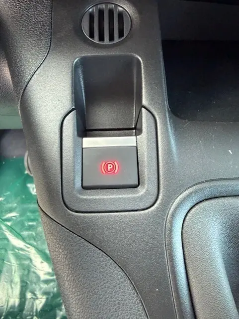 Gros plan sur le bouton de frein à main électronique rouge dans l'habitacle noir du Citroën Berlingo blanc 2026.