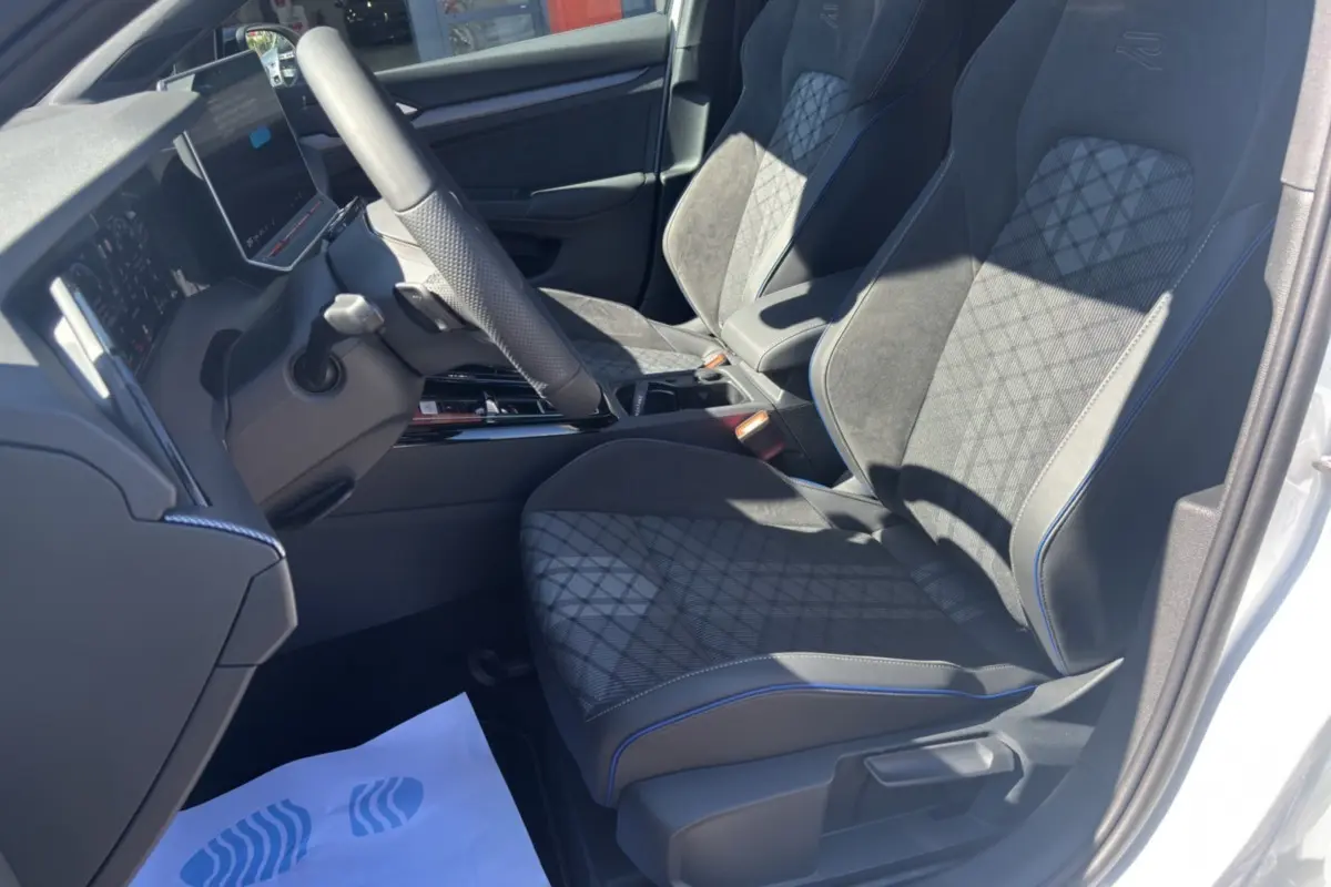 Vue intérieure côté conducteur de la Volkswagen Golf blanche oryx, sièges R-Line en tissu et alcantara avec surpiqûres bleues.