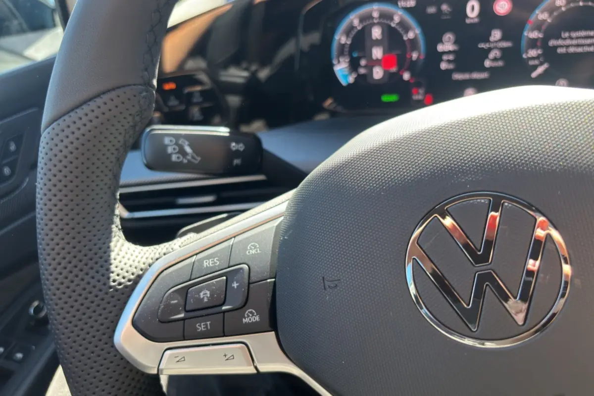 Gros plan sur le volant cuir multifonctions de la Volkswagen Golf TDI 150 R-Line, avec tableau de bord numérique en arrière-plan.
