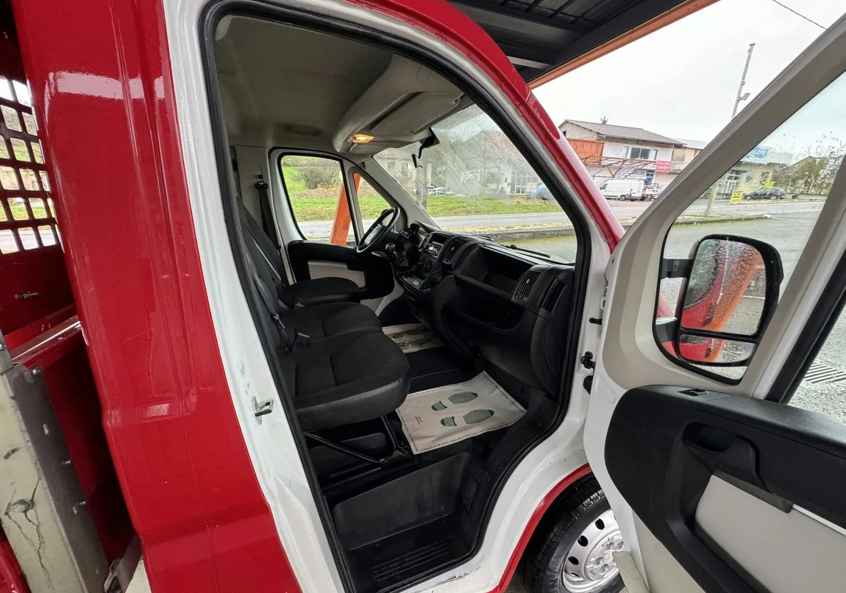 Vue intérieure côté conducteur du Citroën Jumper rouge, montrant les sièges noirs et le tableau de bord fonctionnel.