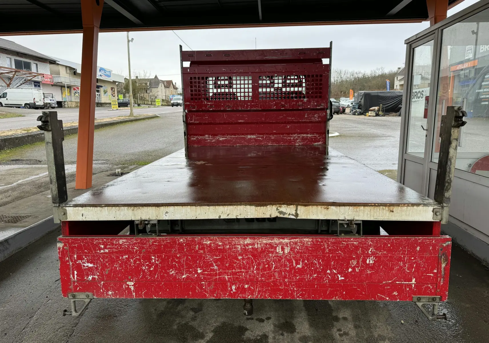 Vue arrière d'une Citroën Jumper benne rouge de 2019 avec ridelles métalliques et plateau usé visible.